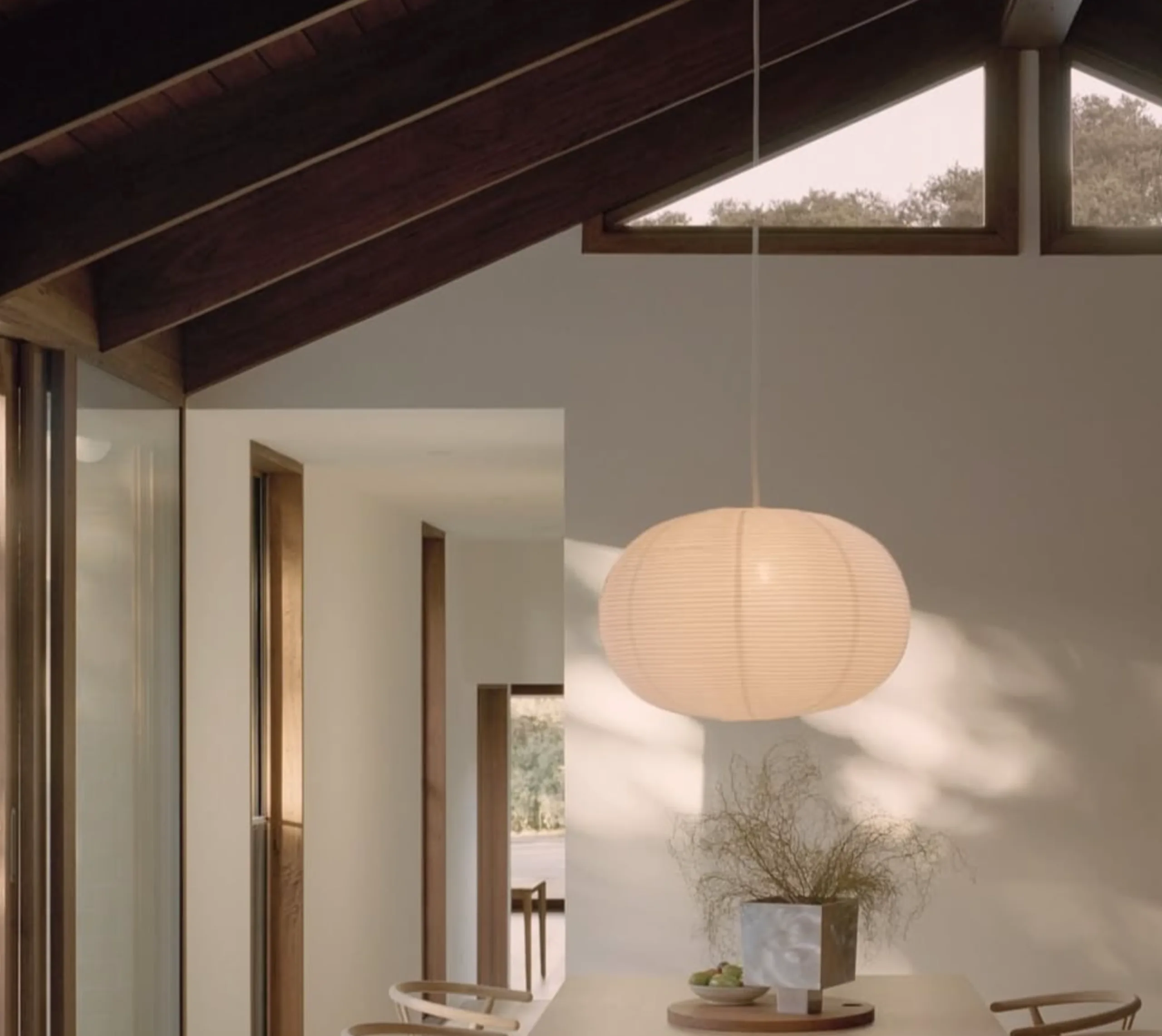 Bureau à domicile aux tons neutres avec un bureau en bois, une chaise blanche, des lampes suspendues et des rideaux beiges.